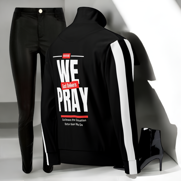 Black women's track jacket with white stripes and "We Pray God Delivers" text on back, paired with black pants and high-heeled boots